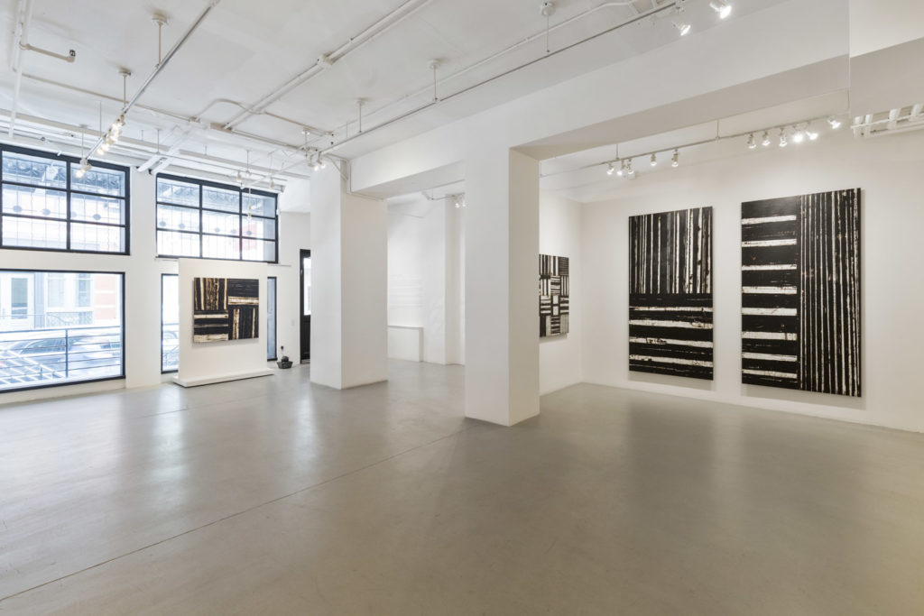 Tribeca gallery with white walls, a polished concrete floor and large black and white paintings under track lighting.