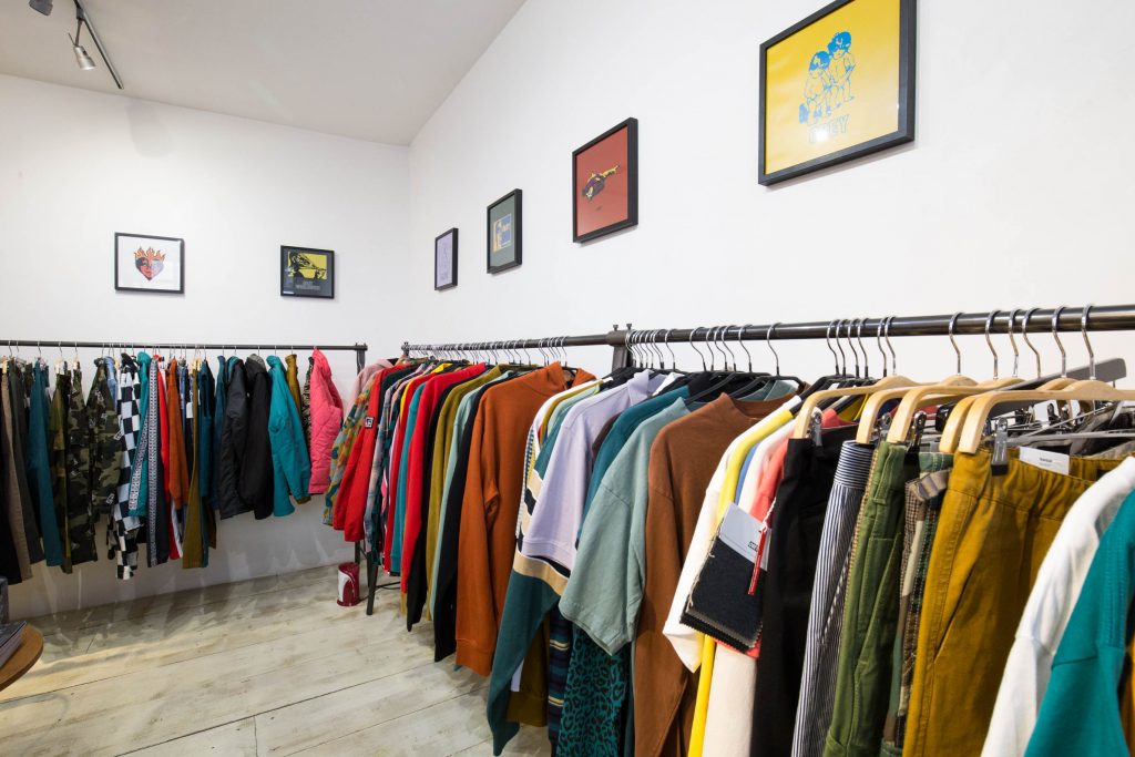 Vintage clothing rails packed with colorful jackets and sweatshirts beneath a row of framed screen prints.