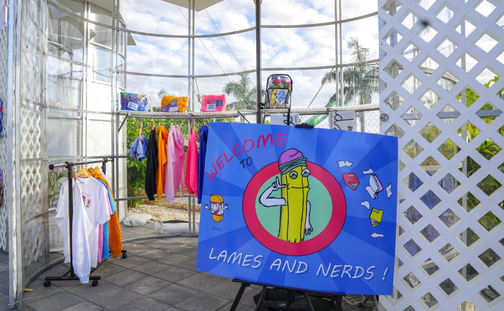 Open-air Miami pop-up with clothing rails and a hand-painted welcome board under a lattice canopy.