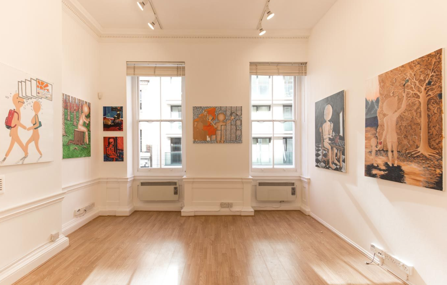 Upper-floor gallery room in Fitzrovia with paintings hung on white walls, track lighting, tall sash windows with period cornicing and a pale wood floor.