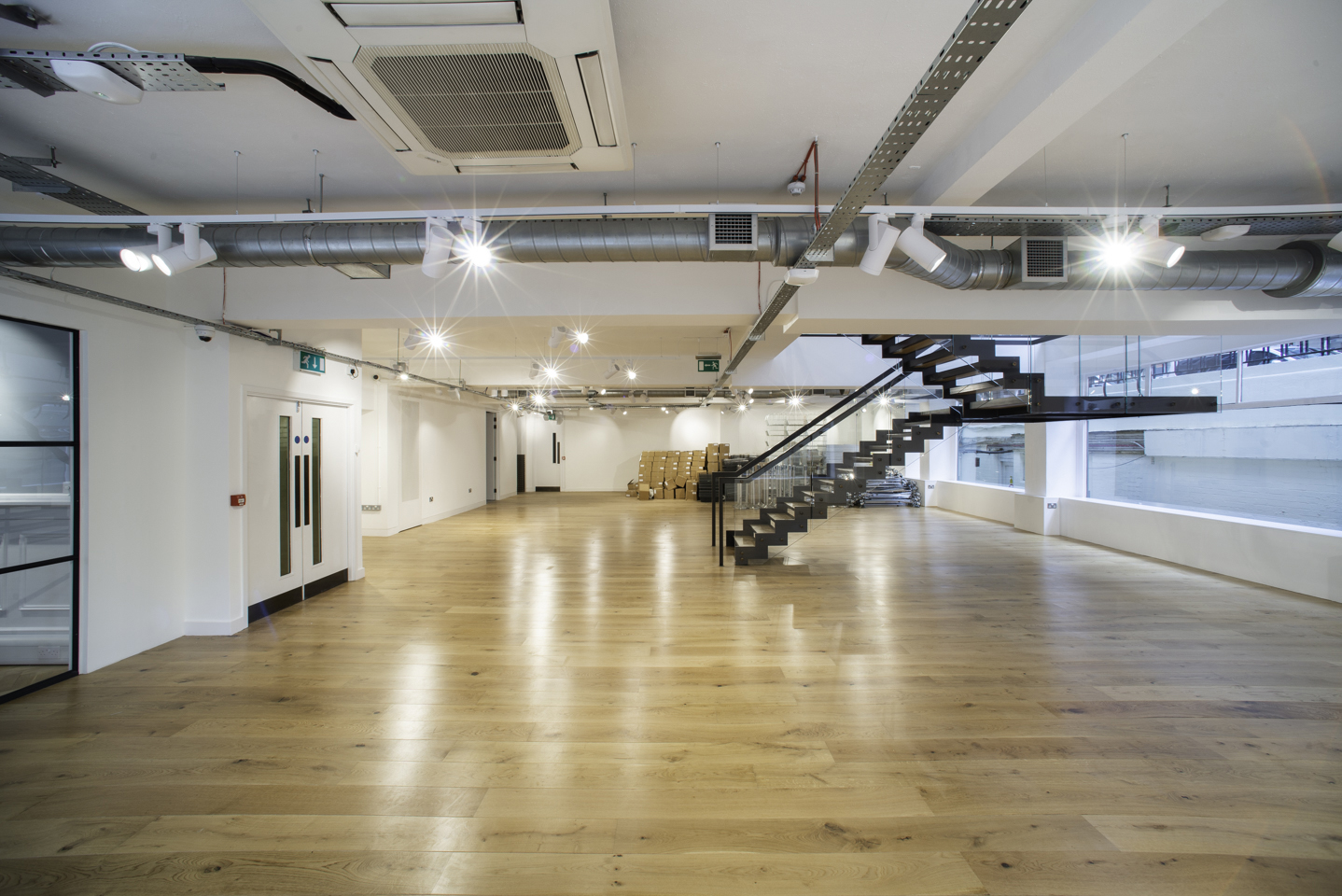 Large open white event floor on Margaret Street in Fitzrovia, with exposed ductwork, a black steel staircase and a wide oak floor.