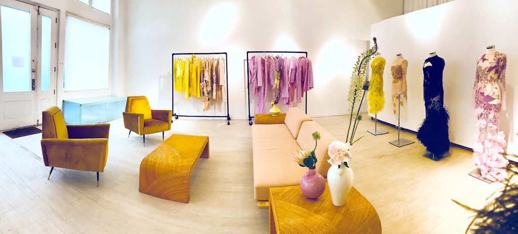 Showroom de vente privée bien agencé, vêtements jaunes et violets sur portants, avec un canapé.