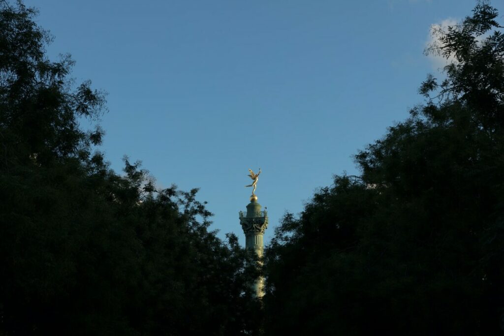 Colonne de Juillet à la Bastille vue à travers les arbres avec monument doré à Paris