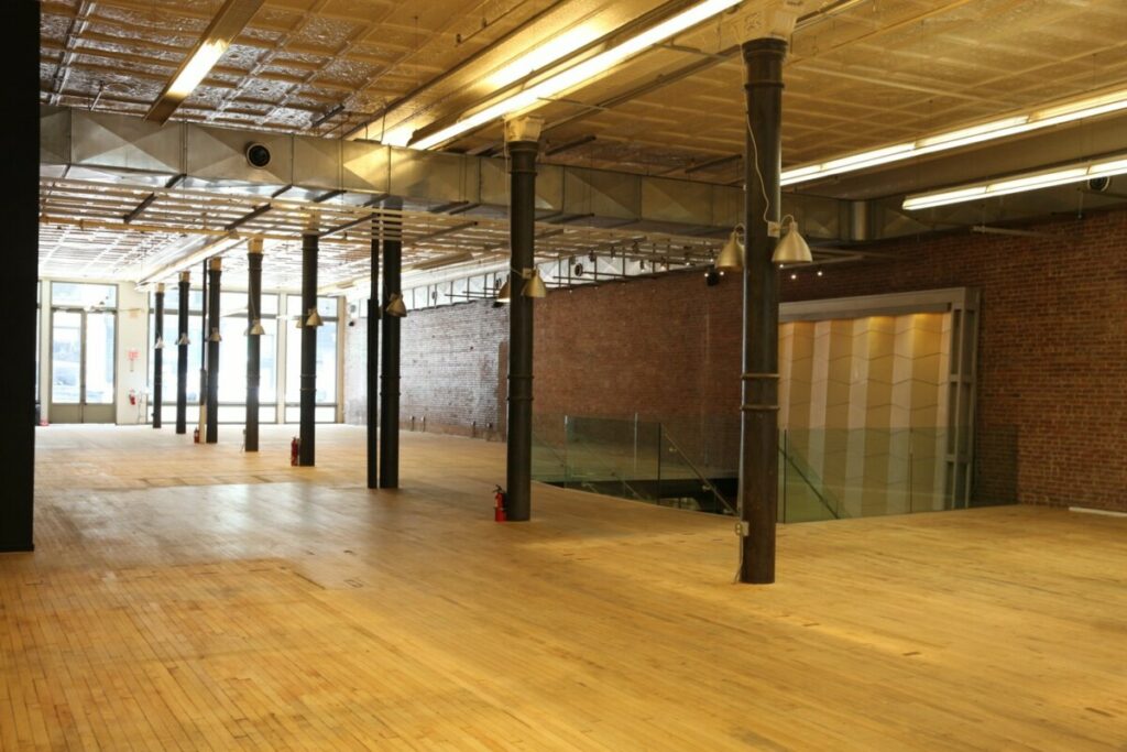 Large loft floor with slim cast-iron columns, a maple board floor, exposed brick and a pressed metal ceiling.