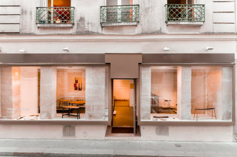 Parisian shopfront with two large display windows either side of a central door, beneath wrought-iron balconies on a stone facade.